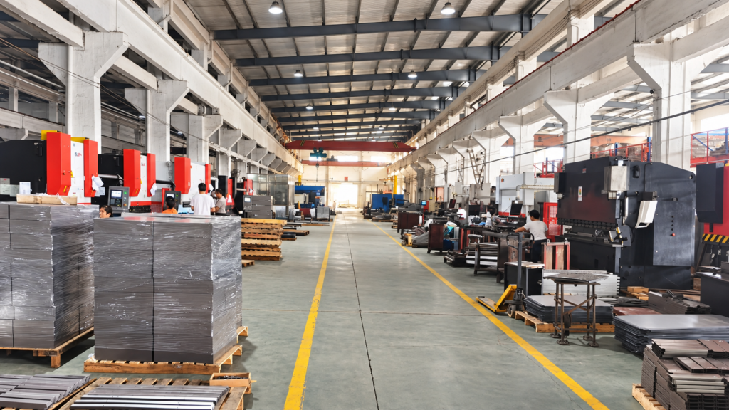 Sheet metal workshop with rows of fabrication machines, workers, and metal parts stacked on pallets beside a central aisle.